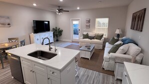 Un salon moderne avec un îlot de cuisine, des meubles blancs et un ventilateur de plafond.