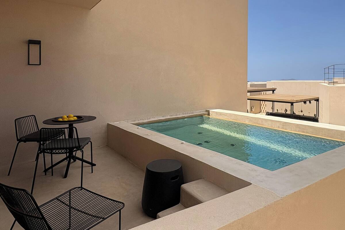 Una piscina en la azotea con una mesa y sillas, un taburete pequeño y un cuadro en la pared.