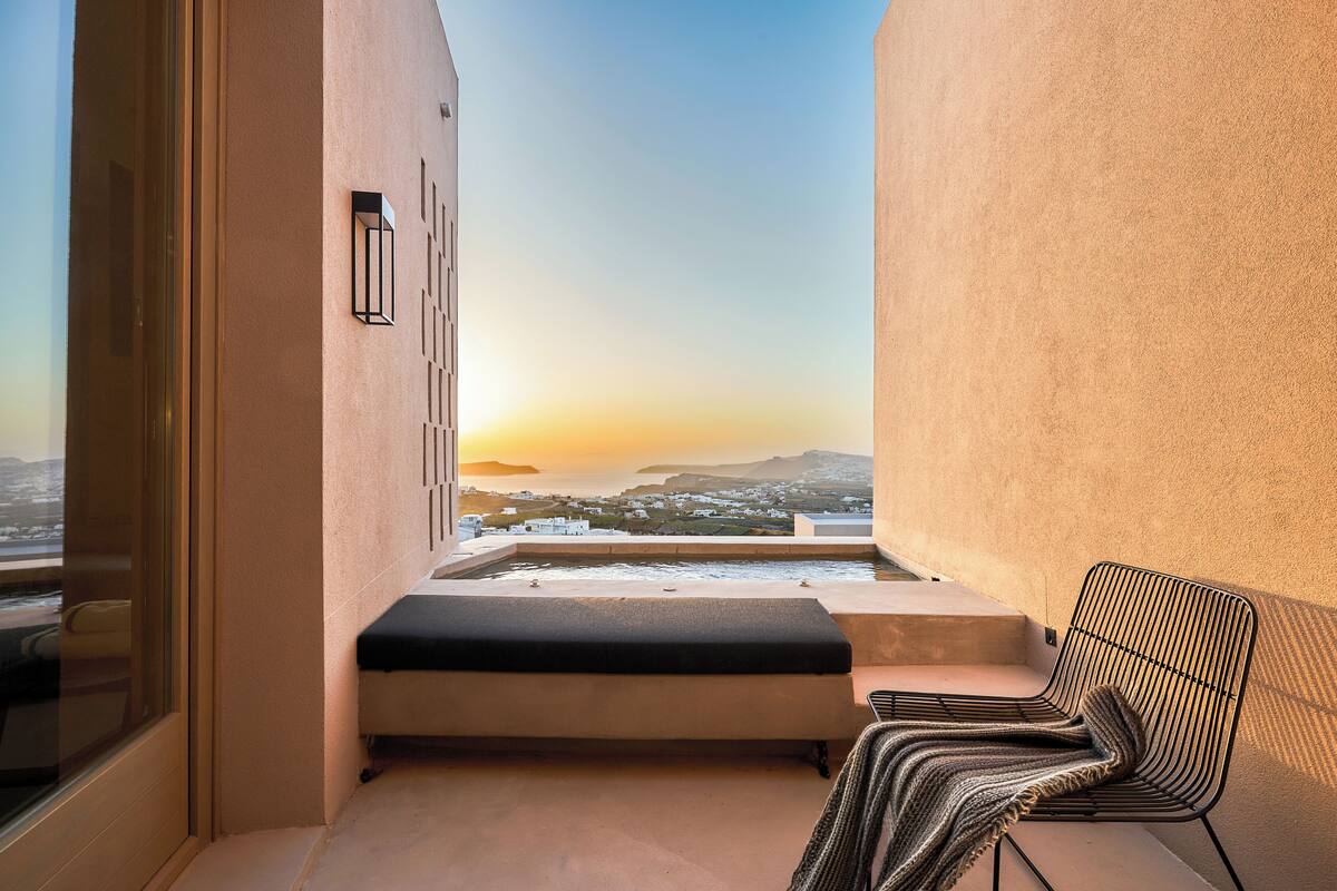 Un balcón con vistas a un atardecer, una banca y una silla.