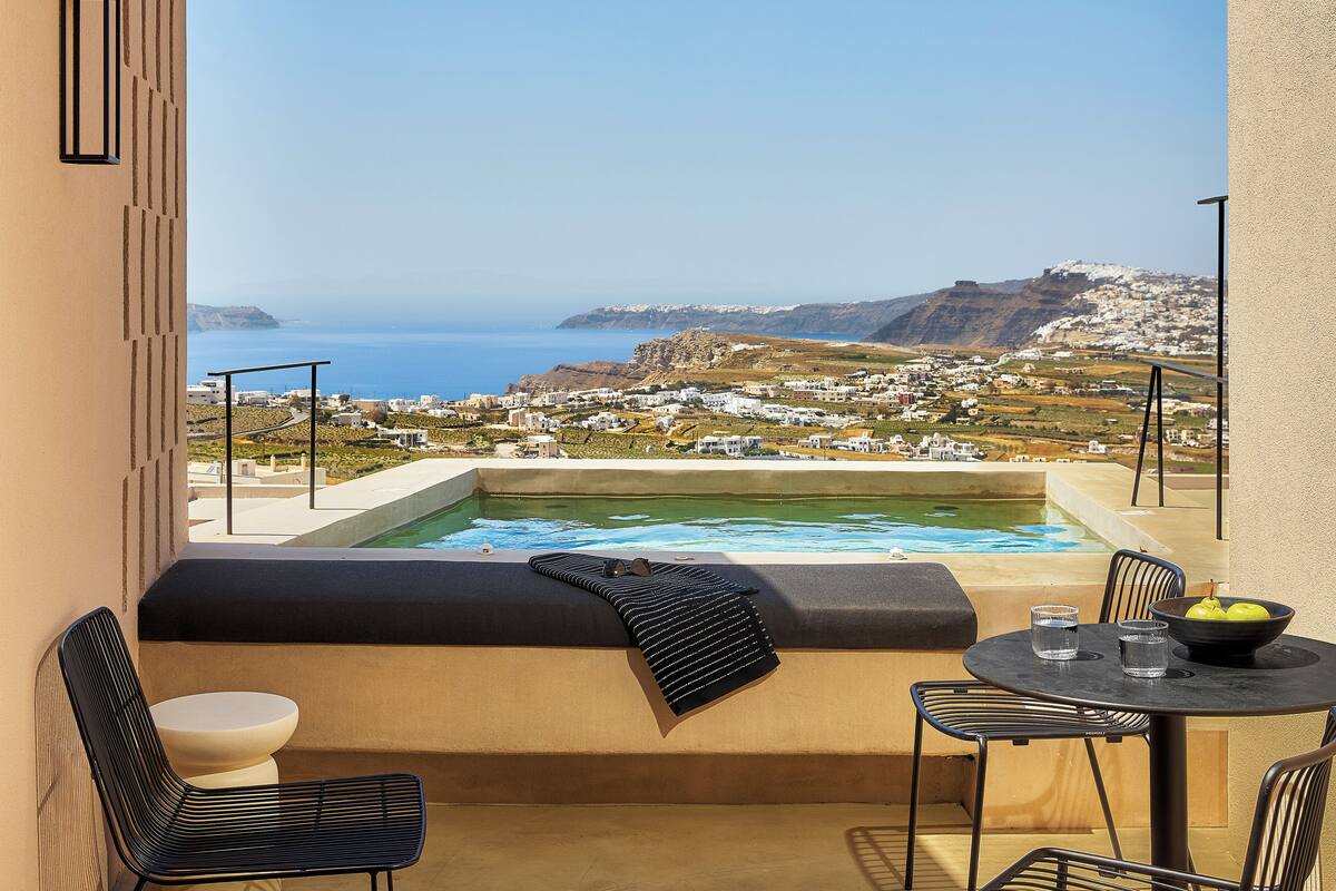 Un balcón con vistas al mar, una bañera de hidromasaje, una mesa con sillas y un cuenco de fruta.