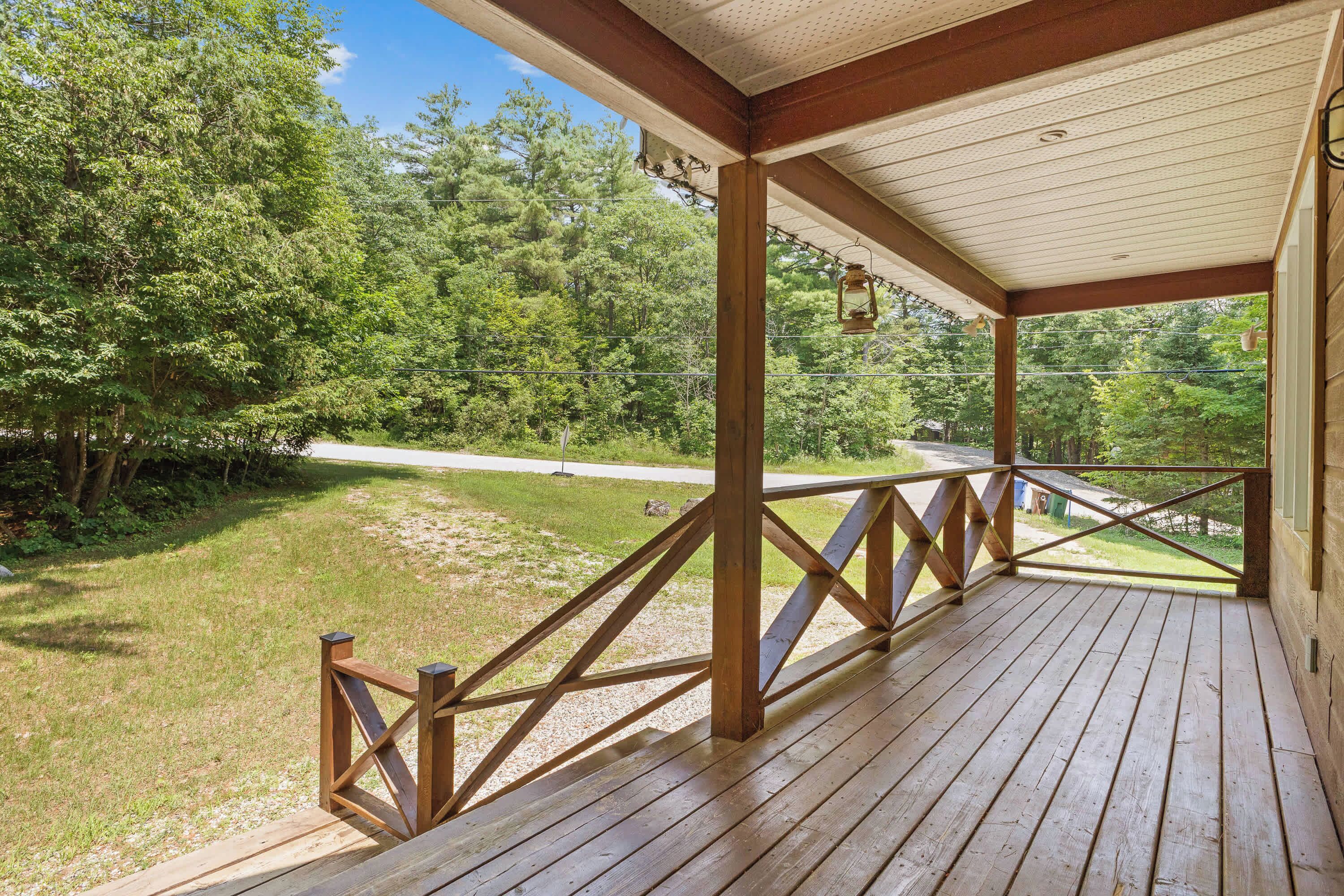 A wooden deck with a railing, overlooking a grassy area with trees.