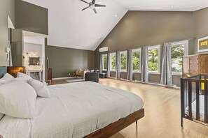 Un dormitorio moderno con una cama grande, un ventilador de techo y vistas al exterior a través de amplios ventanales.