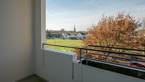 A balcony with a view of a church, a grassy field, and a red car in the distance. - Apartment 'Mk  Delmenhorst 9' with Wi-Fi (Delmenhorst)