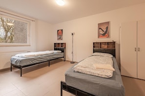 A bedroom with two single beds, a radiator, a window, a floor lamp, and a wardrobe. - Apartment 'Mk Apartments Delmenhorst 1' with Balcony and Wi-Fi (Delmenhorst)