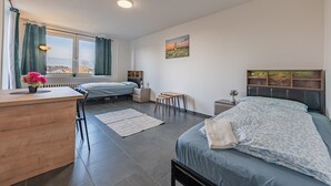Un dormitorio con cama, escritorio, silla, mesita, radiador y ventana con cortinas.