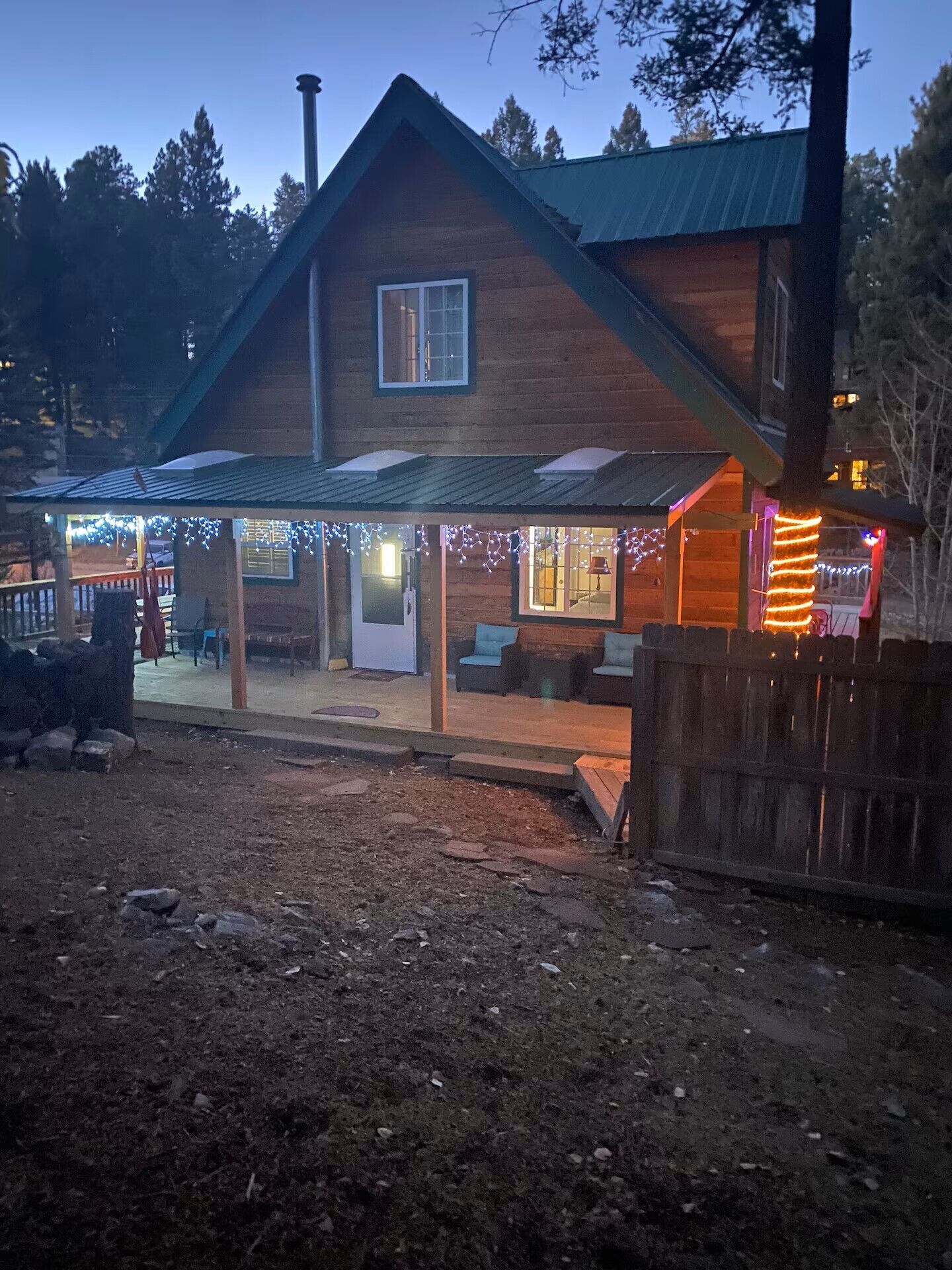 A wooden house with a covered porch, a chimney, and a fenced yard.