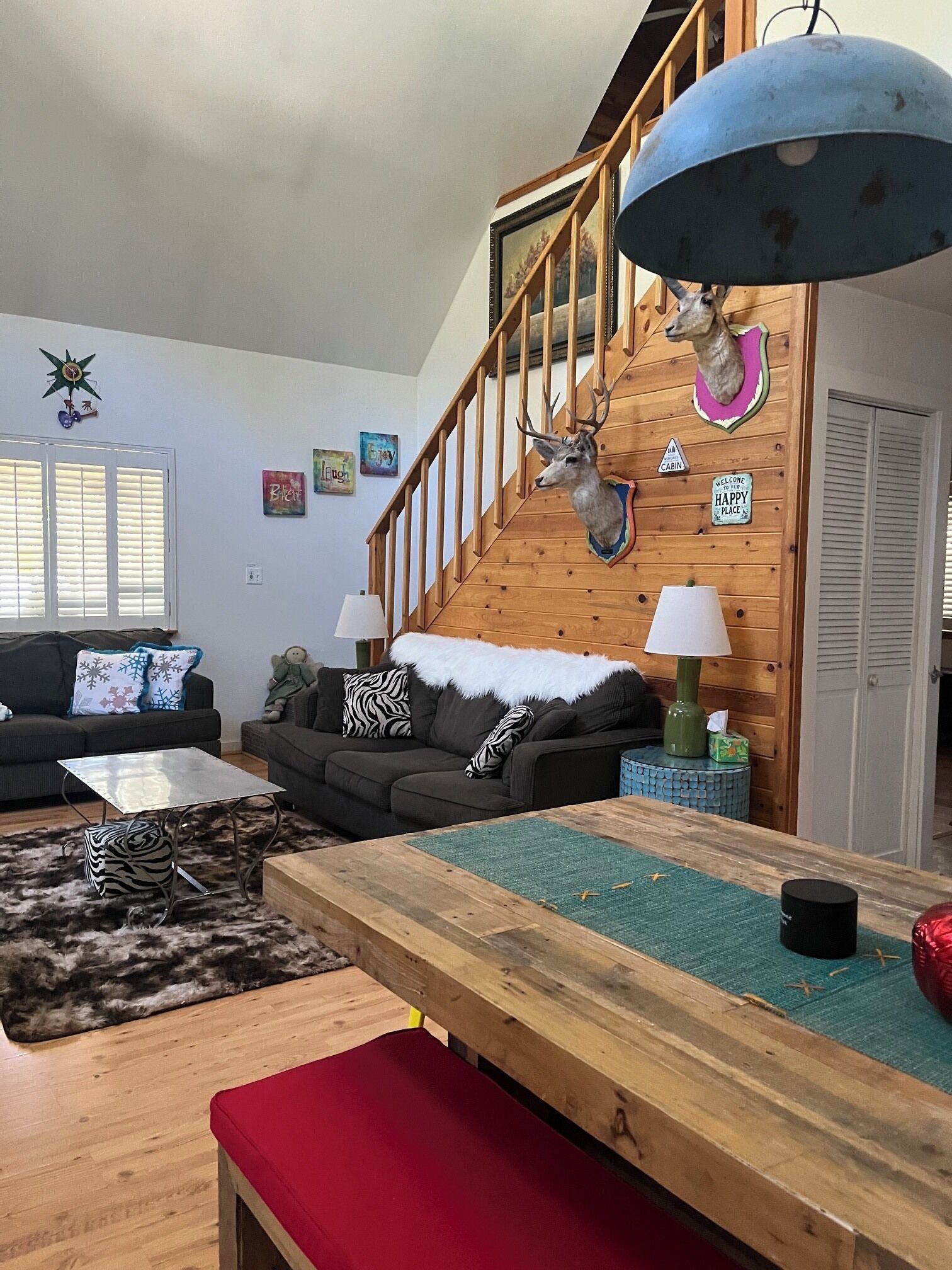A cozy living room with a wooden staircase, a mounted deer head, and a cabin sign.