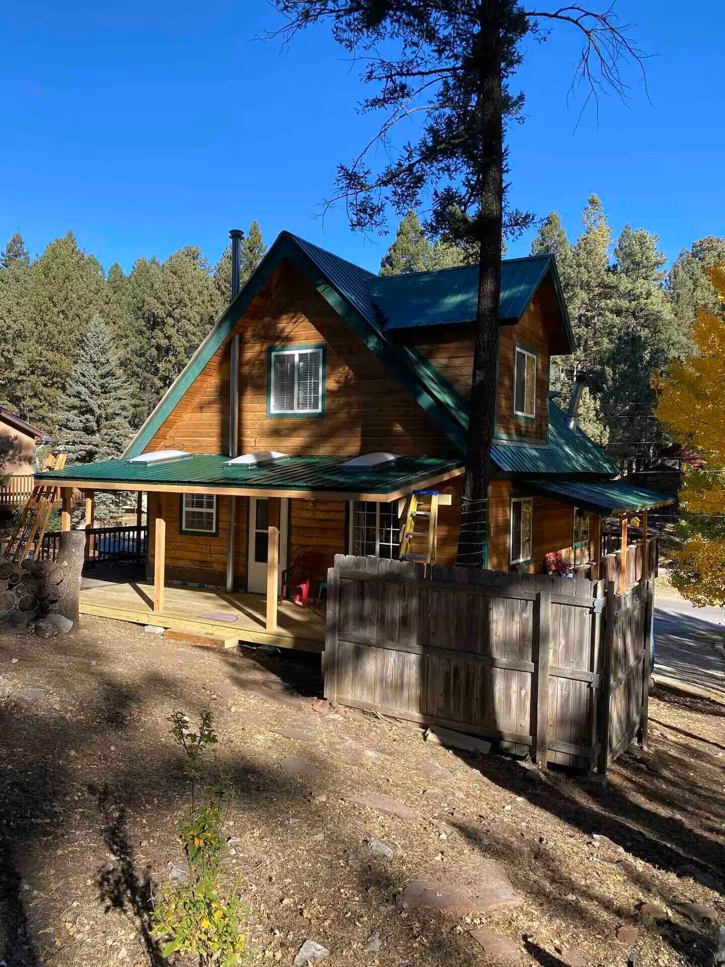 A two-story log cabin with a green roof, a porch, and a fenced yard.