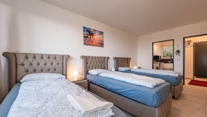 A hotel room with two beds, a painting on the wall, a small kitchen area, and a door leading to another room.