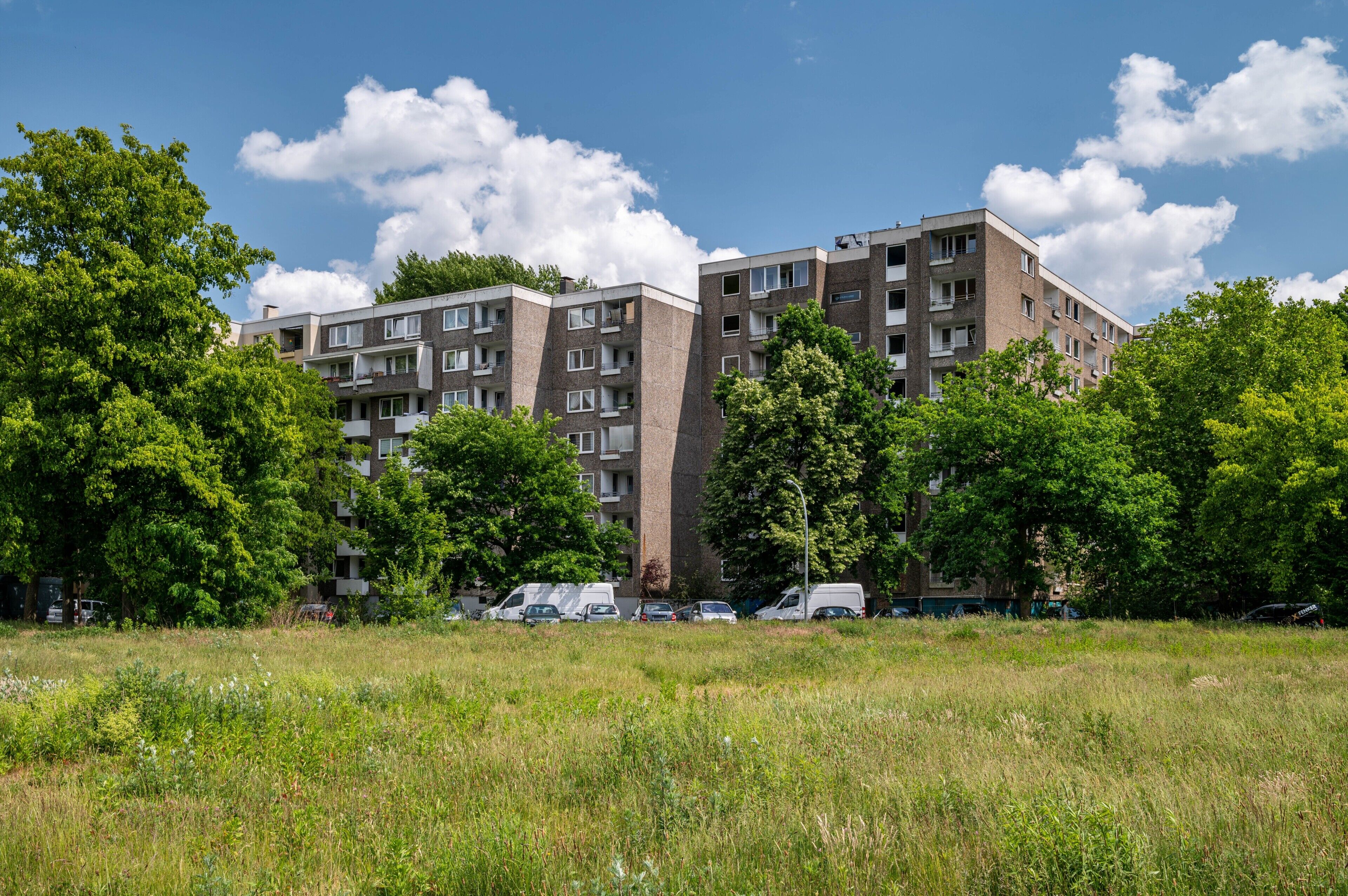 Un immeuble résidentiel à plusieurs étages, doté de balcons, entouré d’arbres et bordé d’un champ d’herbe.