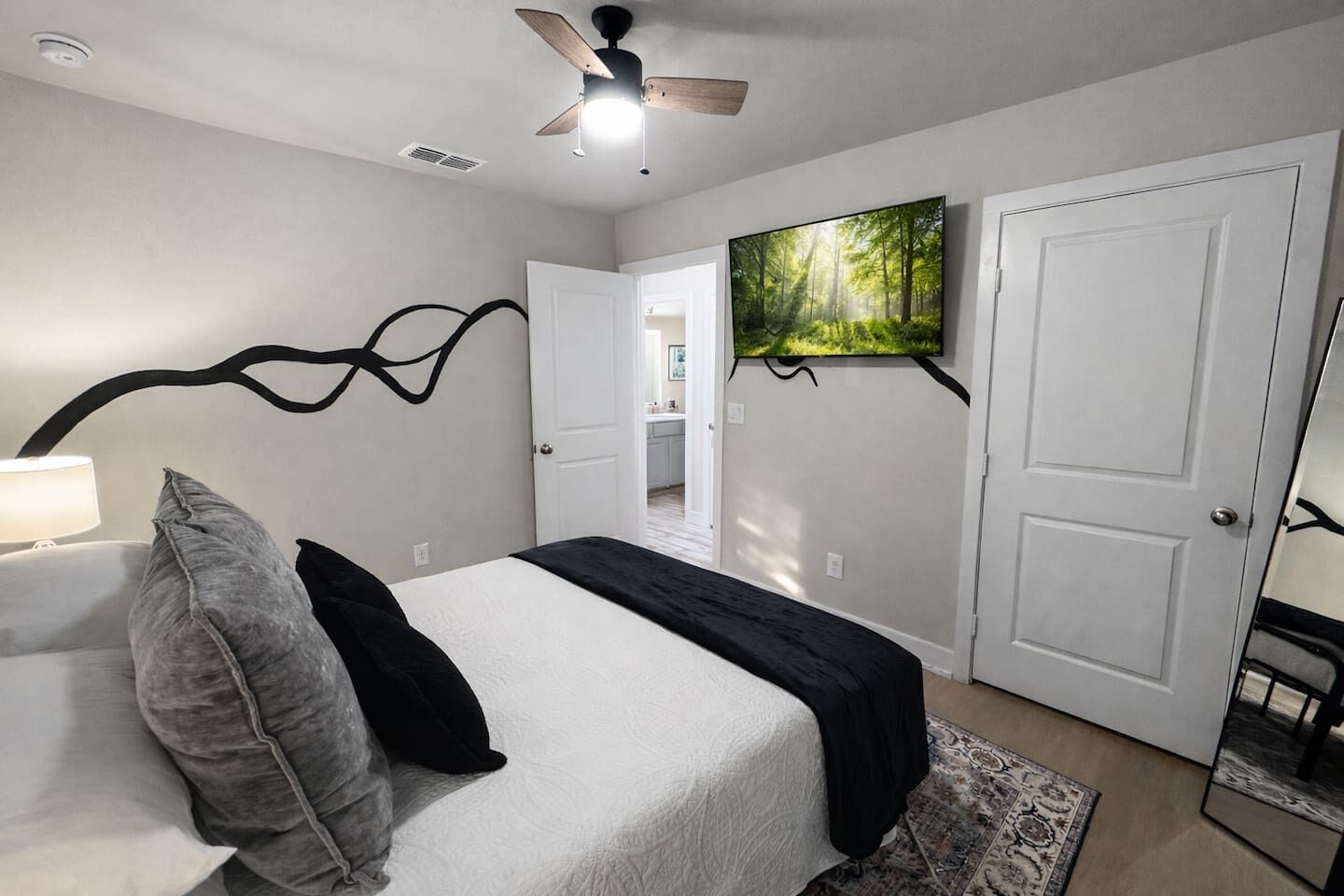 A bedroom with a bed, a ceiling fan, a TV, and a door leading to another room.