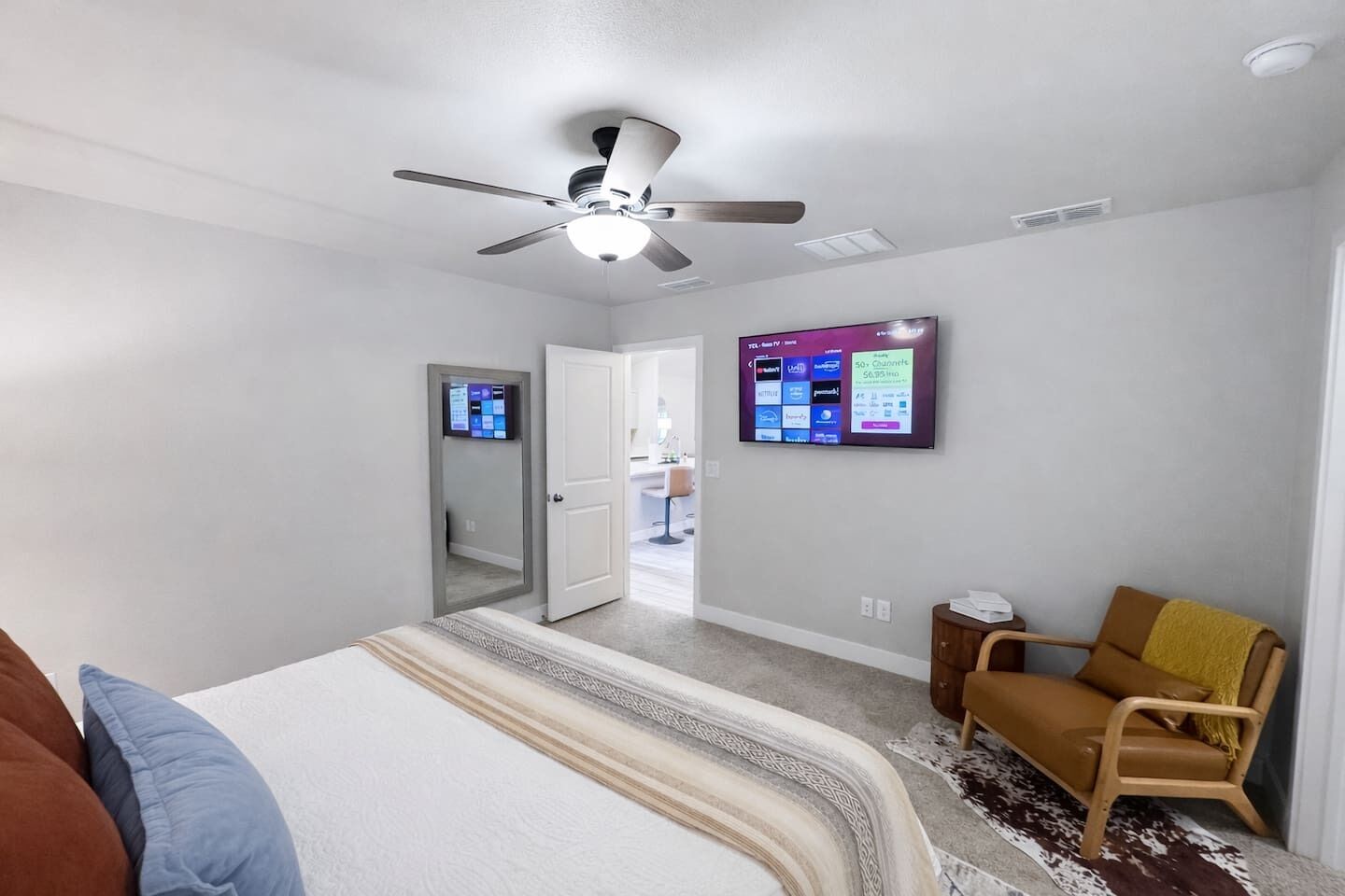 A hotel room with a bed, a chair, a TV mounted on the wall, and a ceiling fan.