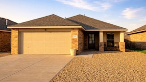 A single-story house with a garage, brick exterior, and a small front yard with gravel. - Urban Cowboy | South Lubbock Retreat • Patio TV (Lubbock)