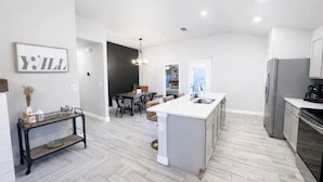 A modern kitchen with a central island, a dining area with a dark accent wall, and a visible living space with a sofa and a coffee table. - Urban Cowboy | South Lubbock Retreat • Patio TV (Lubbock)