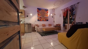 A compact living space with a kitchenette, a sofa, a dining table, and a large abstract painting.