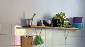 A kitchen with white tiled walls, a gas stove, a wooden cutting board, a red thermos, and a shelf with decorative items. - Cozy little beach house, perfect for family and friends. (Alcobaça)