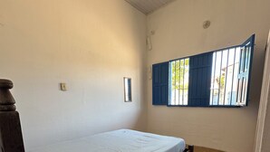 A single bed with a wooden frame and a white mattress, a small rug, and a window with blue shutters. - Cozy little beach house, perfect for family and friends. (Alcobaça)