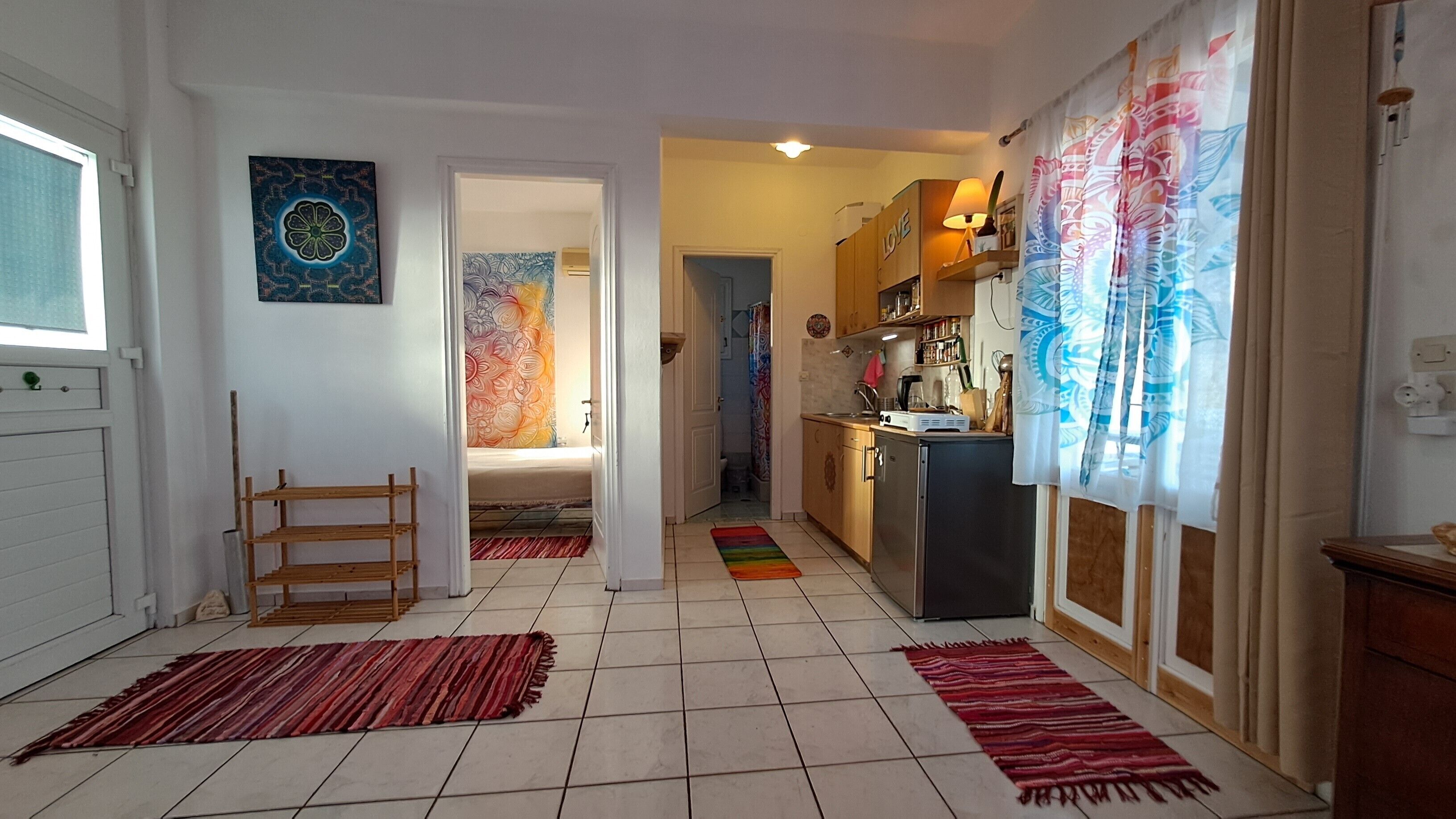 A compact kitchen with a refrigerator, stove, and cabinets. A wooden chair and a colorful rug are on the floor.