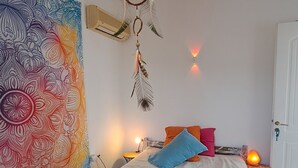 Een slaapkamer met een bed, een kleurrijk wandtapijt, een dromenvanger en een witte deur.
