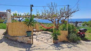 Una propiedad costera con una hamaca, plantas en macetas, una motocicleta y vistas al mar.