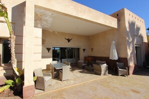 A covered patio area with wicker furniture, a white umbrella, and a bull's head decoration. - Exceptional villa with private pool in Marrakech, Palmeraie area, Atlas view (Marrakech)