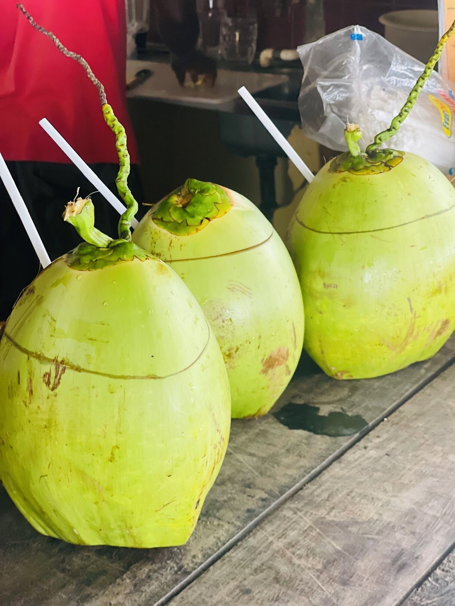 Three green coconuts with straws on a table.