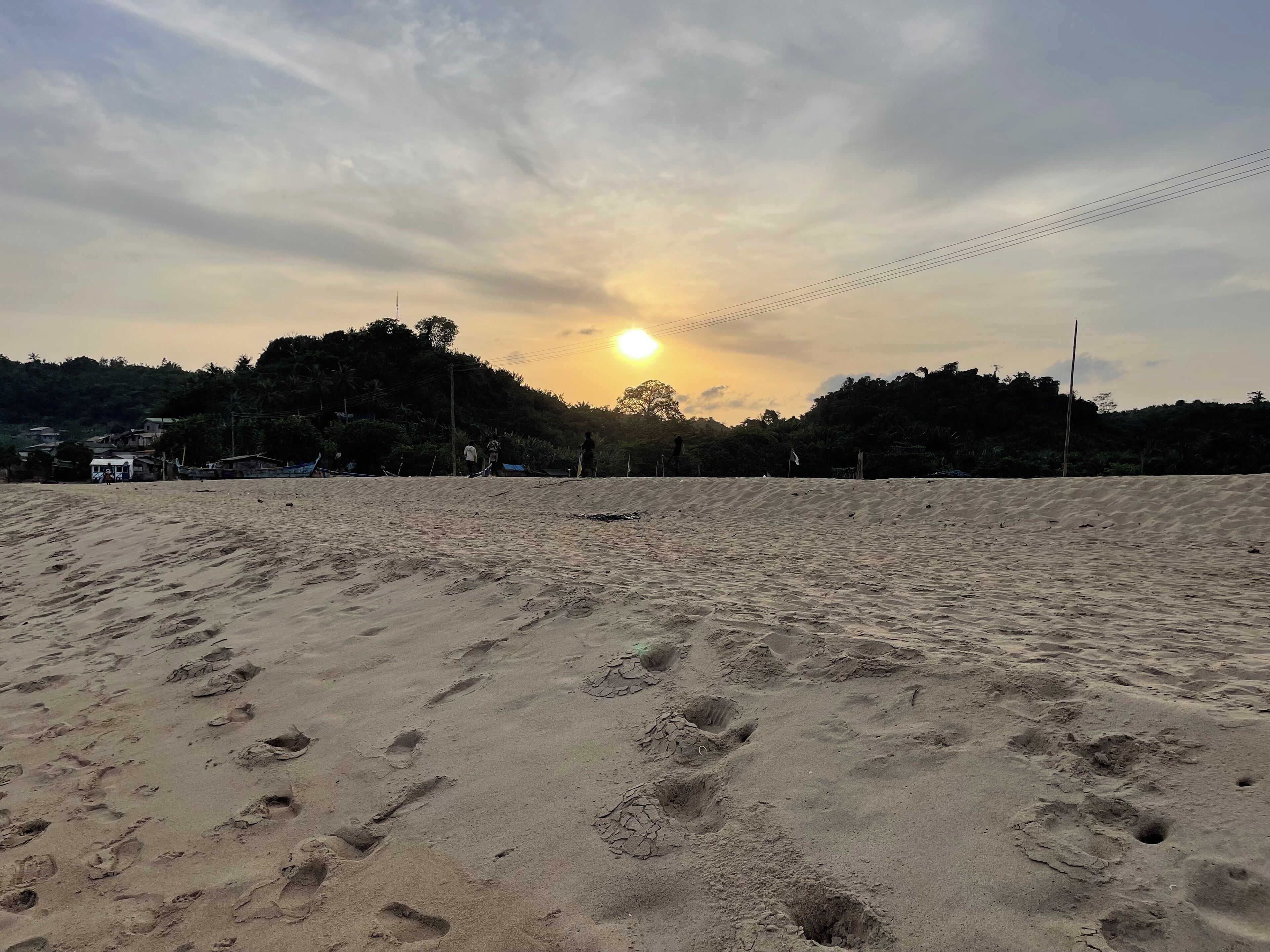 Una playa con huellas y un atardecer de fondo.