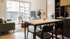 A modern living space with a dining area, a sofa, a TV, and a balcony with a city view. - Stylish 2BR Apt in Providencia with Pool (Providencia)