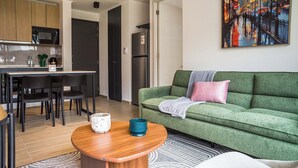 A modern living room with a green sofa, a wooden coffee table, and a painting of a city street. - Stylish 2BR Apt in Providencia with Pool (Providencia)