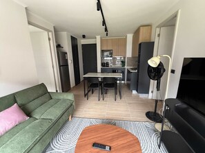 Ein kompakter Wohnbereich mit Sofa, Couchtisch, Fernseher, Essbereich und Küche.