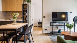 Eine moderne Küche mit Holzausstattung, einem Esstisch mit Stühlen, einem Fernseher auf einem Schrank und einem kleinen Tisch mit einem Blumenstrauß.
