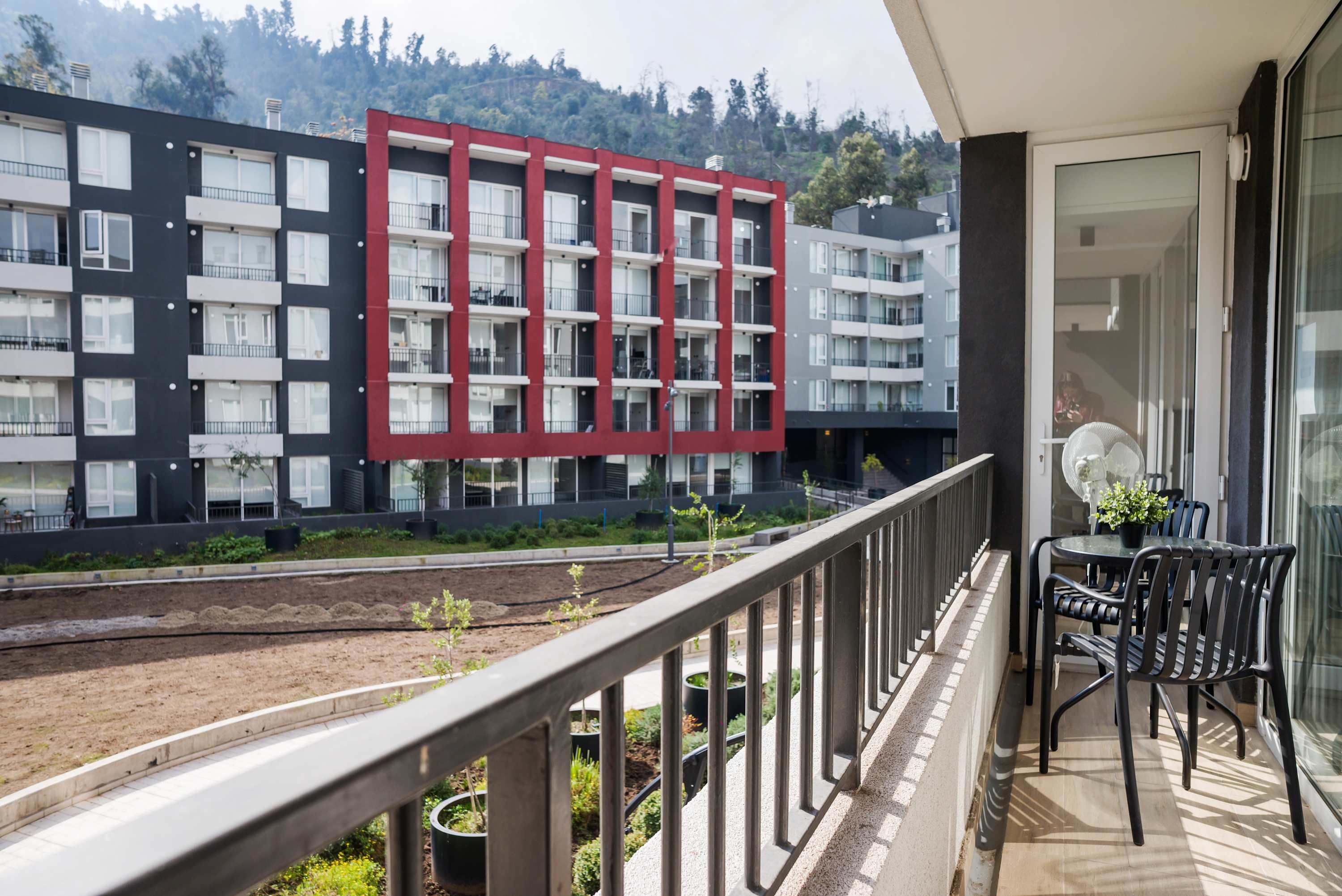 Ein Balkon mit Blick auf ein modernes Gebäude mit mehreren Balkonen, einer kleinen Gartenanlage und einem Esstisch mit Stühlen.