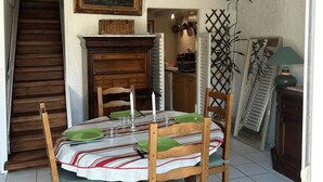 A dining area with a round table set for four, wooden chairs, a fireplace, and a staircase leading to another room. - Beach house at the foot of the Dunes (Seignosse)