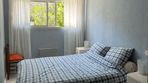 A bedroom with a bed, a nightstand, a chair, and a window with curtains. - Beach house at the foot of the Dunes (Seignosse)