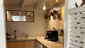 A compact kitchen with wooden cabinets, a dishwasher, and a countertop with a coffee maker and pots. - Beach house at the foot of the Dunes (Seignosse)