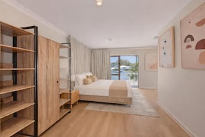 A bedroom with a bed, a wooden wardrobe, a nightstand, a window with a view, and artwork on the wall.