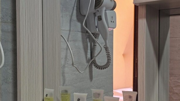 Un bagno con un asciugacapelli fissato alla parete, uno specchio e diverse bottiglie di shampoo su un ripiano.
