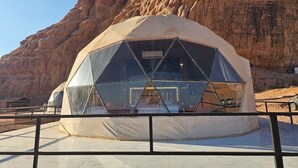 Una tenda a cupola geodetica con interni trasparenti, con sullo sfondo una parete rocciosa.