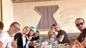 Eine Gruppe von Personen sitzt an einem Tisch in einem Restaurant mit Wandmustern und einer Deckenstruktur.