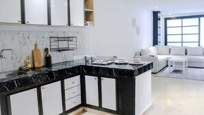 A modern kitchen with black and white cabinetry, a marble countertop, and a dining area with a white sofa and coffee table. - Studio Central in Maarif  (Casablanca)
