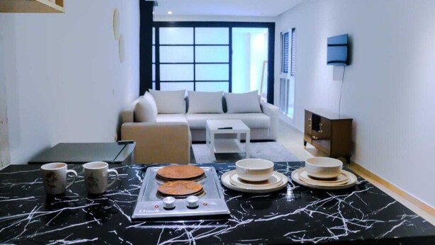 A modern living room with a sofa, a coffee table, and a dining area with a black marble table and plates. - Studio Central in Maarif  (Casablanca)