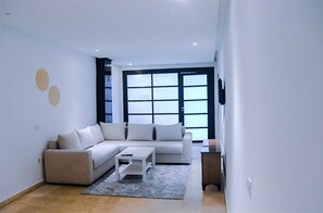 A modern living room with a beige sofa, a white coffee table, and a large window with blinds. - Studio Central in Maarif  (Casablanca)