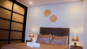A neatly made bed with a brown headboard, two bedside lamps, and a wall with circular decorations. - Studio Central in Maarif  (Casablanca)