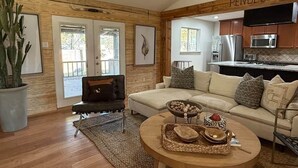 A living room with a sofa, a coffee table with decorative items, a cactus plant, and a kitchen area with wooden cabinets and a microwave. - Pendleton Lodge | Bring Your Boat | Near Lake Conroe (Conroe)