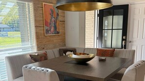 A dining area with a large table, cushioned chairs, a hanging light fixture, and a view of the outdoors. - Pendleton Lodge | Bring Your Boat | Near Lake Conroe (Conroe)