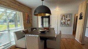 A modern dining area with a large table, cushioned seating, and a pendant light. - Pendleton Lodge | Bring Your Boat | Near Lake Conroe (Conroe)