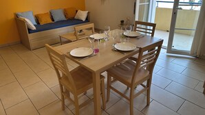 Un coin repas avec une table en bois dressée pour quatre personnes, un canapé avec des coussins et une vue à travers une porte coulissante.