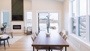A modern living room with a fireplace, a dining table, and large windows.