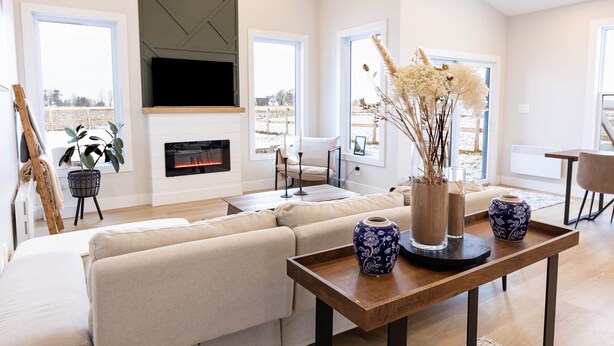 A modern living room with a sofa, a fireplace, a TV, and large windows.