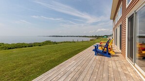 A wooden deck with a view of the water, a grassy area, and a building with large windows. - Red Cliff Escape with Beach Access (Albany)